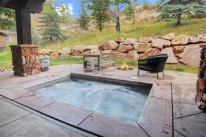 Bubbling hot tub next to an inground fire pit with comfortable seating around the fire and a gorgeous private yard.