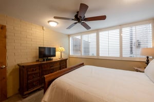 Unwind in the cozy queen bedroom at Park Avenue 211 — complete with a ceiling fan, TV, and warm natural light streaming through the windows.