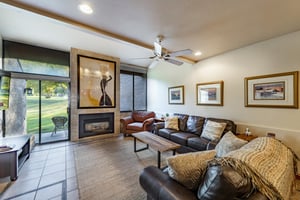 The stylish living room at Park Avenue 245 features rich leather furnishings, a sleek fireplace, and a wall of windows overlooking the outdoors — a refined retreat for your Park City condo rental stay