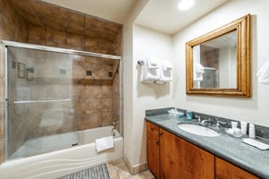 The wellappointed bathroom at Park Avenue 245 features warm stone tile, a combination tub and shower, and a classic woodframed vanity — thoughtful details that enhance the overall Park City vacation