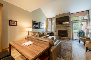 The open living and dining area at Park Avenue 256 showcases a beautiful stone fireplace, vaulted ceilings, and warm wood accents — a refined and comfortable space that elevates the Park City condo re