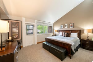 The spacious and elegantly appointed primary bedroom at Park Avenue 256 features vaulted ceilings, a rich wood bed frame, and private door access — a luxurious sanctuary within this premier Park City