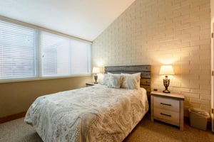 The serene and elegantly appointed bedroom at Park Avenue 256 features a charming brick accent wall, warm bedside lighting, and a plush queen bed — a restful haven within this premier Park City vacati