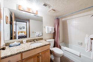 Fresh, clean, and thoughtfully stocked, this full bathroom at Temptation 8 features warm granite countertops, wood cabinetry, and a tub and shower combo — all the essentials for a comfortable Park Cit