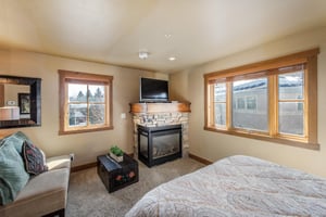 The bedroom at Jupiter Inn 17 features a cozy corner fireplace, flatscreen TV, and abundant natural light — a luxurious touch that sets this Park City vacation rental apart.
