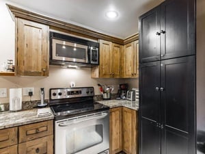 The kitchen at Jupiter Inn 18 features granite countertops, warm wood cabinetry, and modern appliances, giving you everything you need for a comfortable and convenient Park City vacation rental stay.