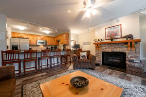 Gather around the stone fireplace in the cozy living area at Resort Plaza 5022 — a standout Park City vacation rental with rustic charm and an open flow to the kitchen.