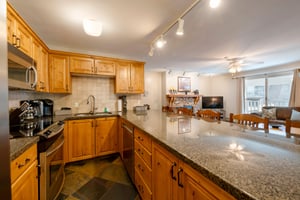 Resort Plaza 5022 features a spacious kitchen with granite countertops and warm wood cabinetry, flowing seamlessly into the dining area — a perfect Park City vacation rental for group gatherings.