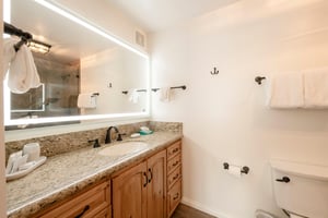 This clean and modern bathroom features warm wood cabinetry, granite countertops, and a beautifully lit vanity mirror, offering a bright and refreshing space to start your day at this Park City vacati