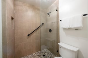 This elegant walkin shower features warm neutral tilework, a pebble stone floor, and sleek matte black fixtures, offering a spalike experience during your Park City vacation rental stay.