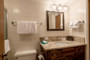 This charming bathroom features warm wood cabinetry, granite countertops, and classic tile detailing, providing a clean and comfortable space for guests during their Park City vacation rental stay.