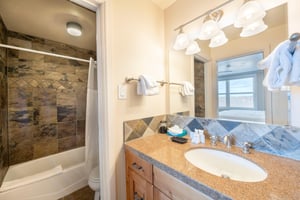 Resort Plaza 5052 continues to impress with another beautifully appointed bathroom, featuring warm stone tile accents, a generous vanity, and a combination tub and shower that add a touch of spalike