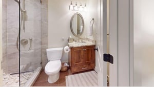 Three Kings 64 impresses with a beautifully designed bathroom featuring warm wooden cabinetry, a elegant oval mirror, and stunning marble tile accents that add a touch of spalike luxury to this excep