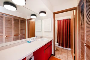 The spacious bathroom at Park Avenue 267 features a large vanity, louvered wood cabinet doors, and a separate shower and toilet area.