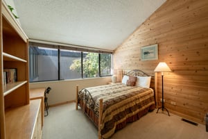 Unwind in the charming guest bedroom at Park Avenue 292.  This comfortable Park City lodging choice features warm wood walls, a cozy iron bed frame, and serene tree views.