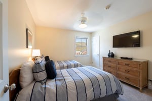 Cozy and wellappointed, this guest bedroom at Resort Plaza 5004 offers a comfortable retreat — this room features a flatscreen TV, modern dresser, and a bright window with lovely mountain views.
