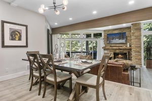 Gather around this elegant dining table where natural light pours through expansive windows, and the warmth of the stone fireplace creates an inviting atmosphere for your memorable meals together.