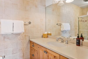 Bright ensuite vanity at Resort Plaza 5064 with warm wood cabinetry, granitelook countertop, and a large mirror for easy prep before hitting the slopes.
