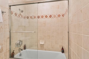 Guest bathroom at Resort Plaza 5064, featuring a deep soaking tub with a sliding glass shower door and classic tile accents.