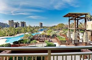 The winding lagoon pool nestled between a spacious wooden deck with seating in the foreground and a deepblue lake in the distance