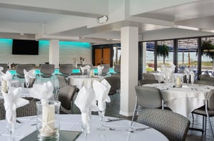 Elegant tables next to beachfacing windows and the bar in the event space at Bilmar Beach Resort