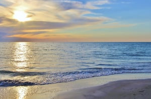 The sun setting over the Gulf as waves lap the shore.