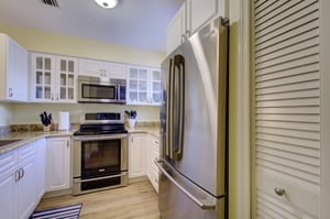 A second view of the updated kitchen at 406 Harbour Oaks, showcasing stainless appliances, granite countertops, and glassfront cabinetry perfect for vacation cooking.