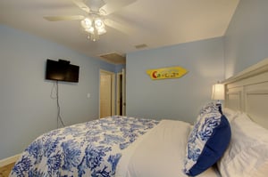 Guests can wind down with their favorite shows in this inviting queen bedroom, complete with wallmounted TV, ceiling fan, and a splash of playful coastal flair.