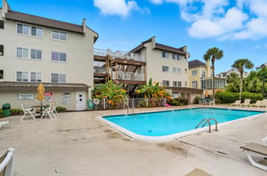 The Shipwatch courtyard features a spacious pool surrounded by palms and lounge seating, just steps from your stay.