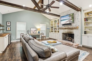 Exposed wood beam ceiling, stone fireplace, full builtin bookshelves flanking the TV, and a sectional sofa big enough for everyone — this is the room people come back for.