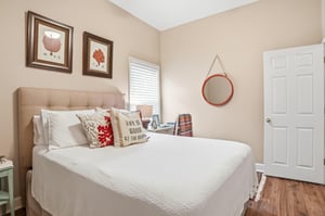 The full room from a wider angle — a round mirror, a bright white door, and warm natural tones throughout.