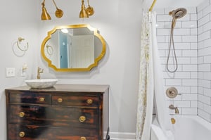 Brass sconces, gold oval mirror, and the walkin shower beyond — the full picture of this standout bathroom.
