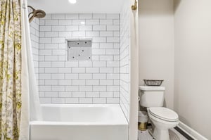Tub and shower behind a botanical curtain, flanked by white subway tile — classic bones with a distinctive finish.
