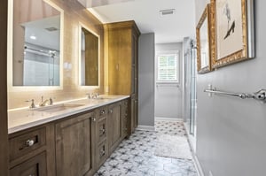 Goldframed mirrors, warm wood tones, and the walkin shower beyond — a bathroom that delivers on the primary suite promise.