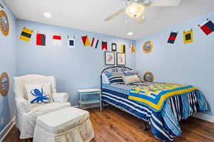 The full nautical room with pennant garland circling the ceiling, light blue walls, and a ceiling fan — it earns the theme.