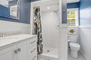 Navy accent wall, mosaicframed mirror, white vanity, and a subway tile tubshower — the hall bath matches the nautical rooms energy.