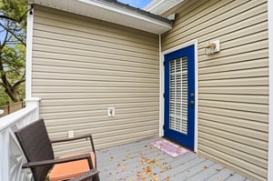 The rear of the home — a blue back door that mirrors the front, a private deck, and green everywhere you look.