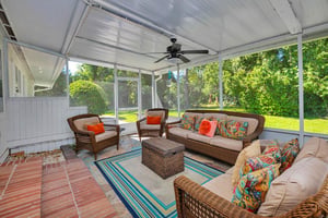 Screenedin porch at 530 Delegal showing multiple seating areas, ceiling fan, and views across the yard from the main house living room.
