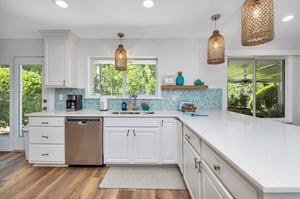 View of the main house kitchen at 530 Delegal showing extended countertop workspace, cabinetry, sink area, dishwasher, and windows looking toward the screened porch.