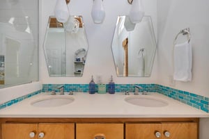Primary bathroom at 530 Delegal showing a dual vanity with two sinks, wood cabinetry, tiled backsplash, mirrors, and wallmounted lighting.