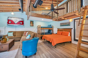 Interior of the guest house at 530 Delegal showing the combined living and sleeping area with bed, bunk beds, seating, lofted space, and wood floors.