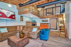 Interior of the guest house at 530 Delegal showing the living area, bed, bunk beds, ladder access to the loft, and open upperlevel railing.