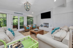 Additional view of the main house living room at 530 Delegal showing seating arranged around the fireplace and television, with glass doors leading to the screened porch.