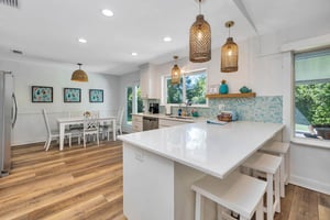 View of the main house kitchen at 530 Delegal showing island seating, countertop workspace, cabinetry, pendant lighting, and the dining area beyond.