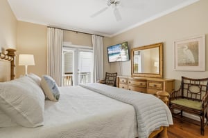 Main floor king primary suite with hardwood floors, mounted TV, and French doors to the covered balcony.