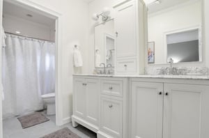 Ensuite bathroom for the main floor king primary suite with double vanity, granite counter, and a tubshower area nearby.