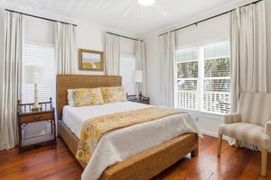 Main floor queen bedroom with hardwood floors and corner windows bringing in natural light.