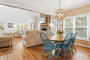 Wide mainlevel view with dining area, living room seating, stone fireplace, and kitchen sightlines all connected.