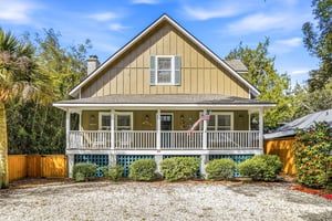 Front exterior view with gravel drive and parking beneath and beside the elevated cottage.