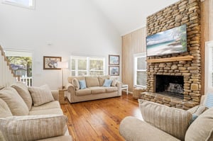Main living room centered around the fullheight stone fireplace, with hardwood floors and comfortable gathering space.